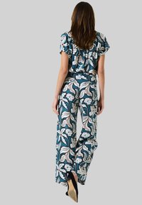 Tweekleurige outfit met bloemenpatroon in teal met witte en rode accenten. Gerimpelde korte mouwen en brede broekspijpen, gemaakt van zachte stof.