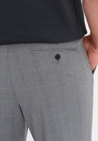 Pantaloni grigi a spina di pesce con un sottile motivo a quadretti gialli, dotati di una tasca posteriore piatta chiusa da un bottone nero. Il tessuto è liscio e ha una vestibilità su misura.