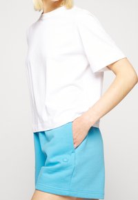 Vit bomull t-shirt med korta ärmar, parat med blå bomullsshorts med en sidoficka och en subtil broderad logotyp.