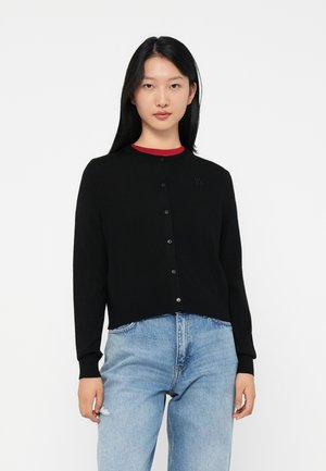 Black knit cardigan with a round neck and button closure. Features a subtle logo on the chest and long sleeves, paired with light blue jeans.