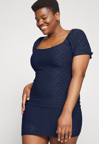 Vestido curto azul-marinho com forma justa, mangas curtas bufantes, decote quadrado e padrão de ilhós texturizado por todo o vestido.