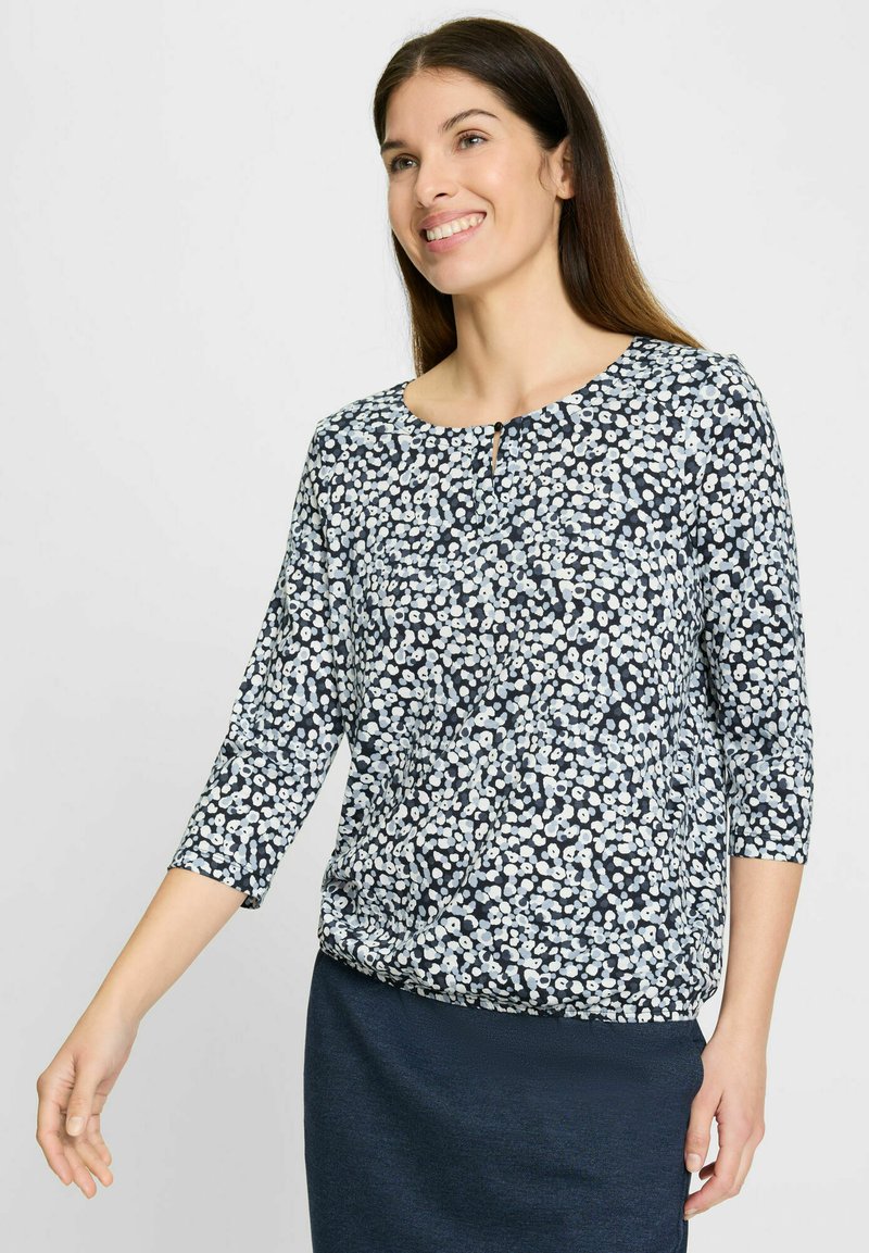 Marineblaue Bluse mit floralem Muster, dreiviertel Ärmeln, Rundhalsausschnitt und einem kleinen Schlüssellochdetail vorne. Weicher Stoff mit strukturierter Haptik.