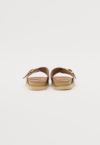 Sandales glissantes brunes avec une finition lisse, dotées d'une large bride et d'une accent en boucle dorée. Semelle légèrement surélevée avec une base couleur crème.