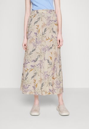 Femme portant une jupe midi beige avec un imprimé floral violet, orange et gris, associée à des chaussures beige sans lacets et un haut bleu.
