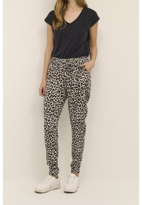 Zwart korte mouwen V-hals top gecombineerd met beige jogger broek met een zwart luipaardprint. Witte sneakers maken de outfit af.