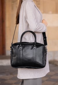 Sort læderhåndtaske med dobbelte håndtag, aftagelig skulderrem og dekorativ syning. Glat tekstur og rektangulær form.