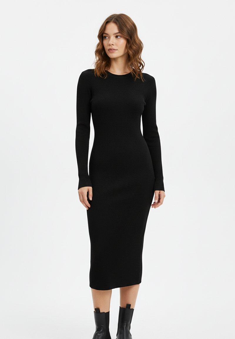 Schwarzes geripptes Midikleid aus Strick mit langen Ärmeln, figurbetonter Silhouette, rundem Ausschnitt und seitlichen Schlitzen, kombiniert mit Stiefeletten.