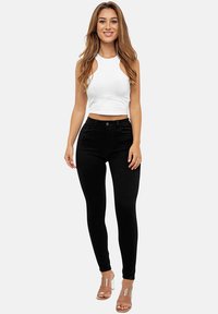 Pantalones ajustados de tiro alto en negro, hechos de una tela elástica, combinados con un top corto sin mangas blanco con cortes en los laterales. Tacones transparentes.