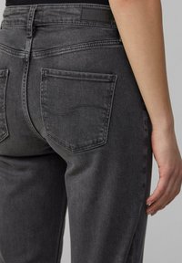 Jean en denim noir à taille mi-haute, doté de deux poches arrière et d'une texture légèrement délavée. Les coutures sont dans une teinte foncée assortie.