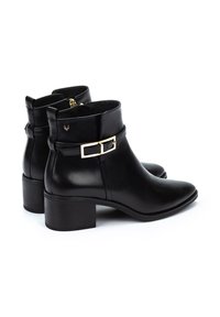 Botas de cuero negras hasta el tobillo con punta afilada, tacón bloque de altura media y un acento decorativo de hebilla dorada en el lateral.