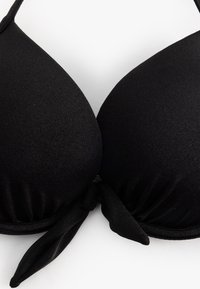 Zwarte bikini-top met gevoerde cups, verstelbare bandjes en een gestrikt knoopdetail in het midden. Gemaakt van een gladde, rekbare stof.