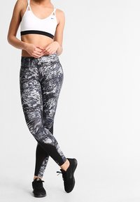 Legginsy w czarno-szary wzór z wysokim stanem i dopasowanym krojem, zestawione z białym strojem sportowym posiadającym czarny pas.