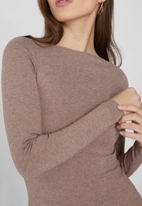 Camiseta de manga larga en color marrón claro, de tejido acanalado con un escote barco, diseño ajustado y textura suave, con detalles de costura sutiles.