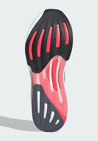 Suela de zapatilla deportiva negra y roja con goma texturizada que presenta surcos y recortes, resaltando un sistema de amortiguación multicolor.