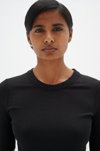 Melnas ribotas garām piedurknēm augšdaļa ar apaļu kakla izgriezumu, ar pieguļošu siluetu un gludu tekstūru, uz vienkārša gaiša fona.