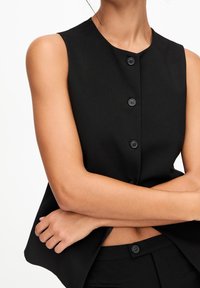 Black sleeveless top with a round neckline, featuring a button front closure and a smooth, tailored fabric texture.