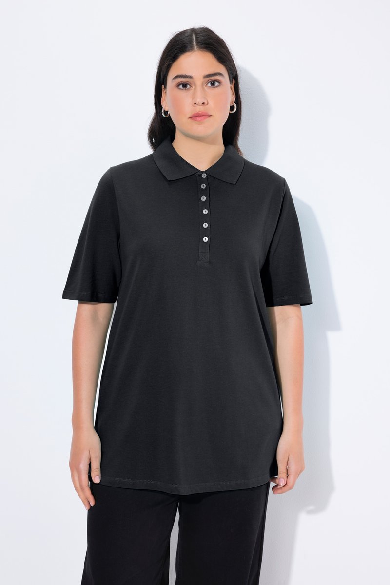 Frau mit glatten dunklen Haaren trägt ein schwarzes kurzärmeliges Poloshirt mit Knöpfen und steht vor einem einfachen weißen Hintergrund.