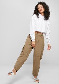 Balta saīsināta kapuce ar garām piedurknēm, kombinēta ar haki krāsas cargo biksēm ar sānu kabatām un sašaurinātām kāju daļām. Valkātas kopā ar baltiem slidīšu sandales.