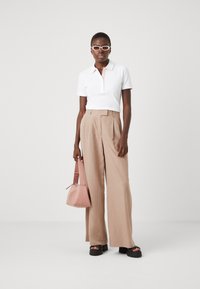 Polo bianco a maniche corte, pantaloni beige a gamba larga, sandali con piattaforma nera chunky e una piccola borsa rosa.