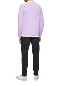 Sweat-shirt long violet à manches longues avec un col rond, associé à un jean noir et des baskets blanches. Coutures visibles et design à ourlet superposé.