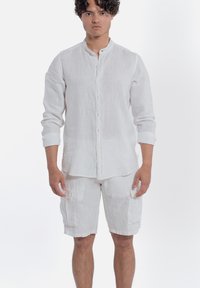 Wit linnen overhemd met lange mouwen, een staande kraag en knopen aan de voorkant, gecombineerd met bijpassende cargoshorts met zijzakken.