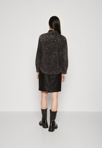 Camicia di denim nera con orlo arrotondato, polsini abbottonati e lavaggio sbiadito. Abbinata a una gonna di pelle nera e stivali alti fino al ginocchio neri.