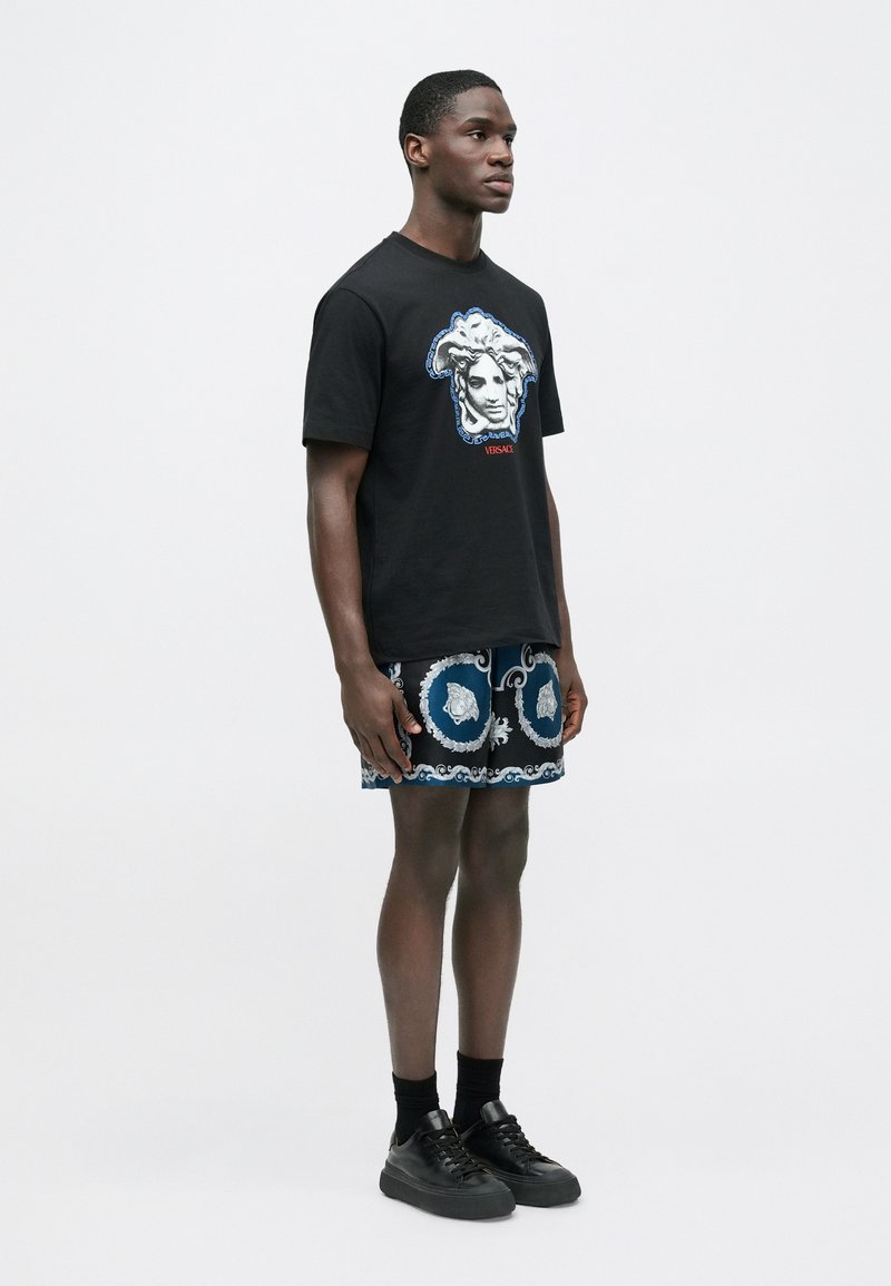 Black t-shirt with graphic design featuring a face, paired with blue patterned shorts. Texture appears smooth, and the style is casual.