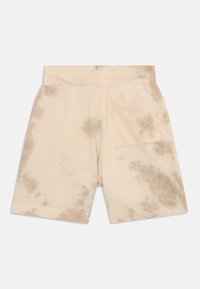 Shorts tie-dye beige en tissu doux, avec une taille large et une poche arrière unique. Motifs bruns distinctifs sur l'ensemble.