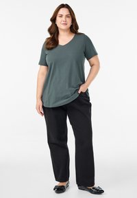 Zelené tričko s V-výstřihem, krátké rukávy, volný střih, spárované s černými kalhotami s širokým střihem. Jednoduchý design, jemná textura a žádné viditelné vzory.