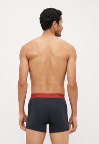 Boxer shorts noirs avec une ceinture bordeaux, en tissu lisse et au design ajusté, vus de l'arrière.