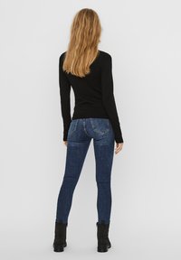 Svart langermet topp kombinert med tettsittende mørkeblå jeans med baklommer og ankelhøye svarte støvletter med glidelås.