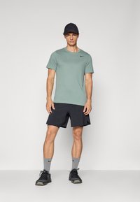 Camiseta ligera verde de Nike, pantalones cortos negros, zapatillas negras, calcetines grises. Diseño simple, cuello redondo, detalle del logo en el pecho.
