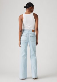 Világoskék, magas derekú farmernadrág, enyhén haranguj, hátul barna bőrpárnázással és két cipzáras zsebbel.