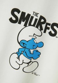 Tela blanca con un personaje de los Pitufos impreso en color azul en una posición de carrera, con texto en negro que dice "LOS PITUFOS" encima.