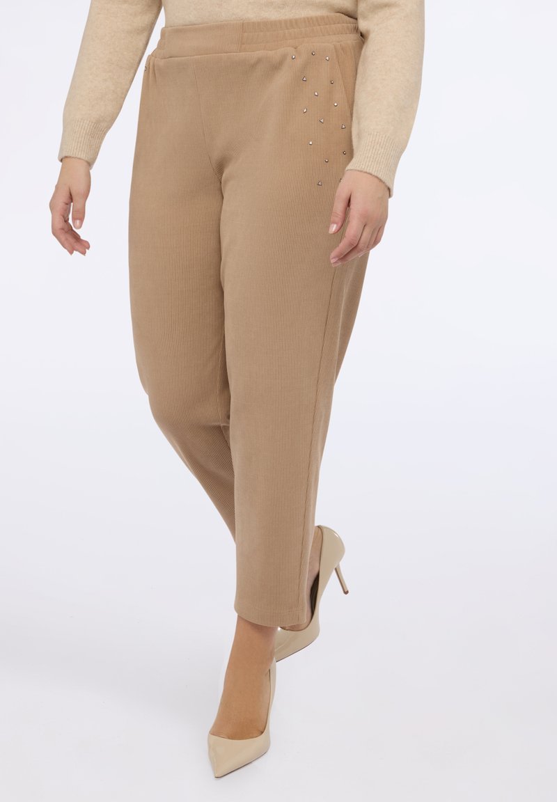 Beżowe, prążkowane spodnie z elastycznym paskiem, z drobnymi srebrnymi ćwiekami po jednej stronie. W zestawie z cielistymi szpilkami.