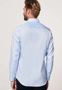 Camisa abotonada de color azul claro con mangas largas, cuello clásico y dobladillo curvado. Fabricada con una tela suave con un brillo sutil.