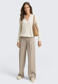 Pulover bej cu guler în V din tricot cu nervuri, pantaloni largi bej și pantofi slip-on crem. Port o geantă de umăr maro deschis. Paletă de culori neutre.