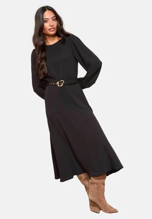 Svart långärmad klänning med ett midjebälte som har ett guldspänne. I kombination med knähöga beige mockastövlar med spetsiga tår.