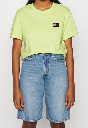 Persoon draagt een felgroen Tommy Jeans T-shirt en lichtblauwe high-waisted denim shorts met voorzakken.