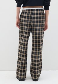 Pantalons large à carreaux noir et beige avec une taille élastique, présentent une coupe décontractée et un ourlet soigné.