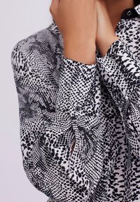 Black and white patterned shirt with a point collar, featuring varying dot and line textures and button details on the cuffs.