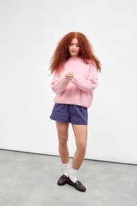 Pulover roz pufoș, pantaloni scurți dungi bleumarin, șosete albe și mocasini negri. Pulover cu croială lejeră, textură în dungi și mâneci scurte.