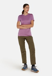 Maglietta viola a maniche corte in tessuto leggero, abbinata a pantaloni verde oliva aderenti, entrambi adatti per attività all'aperto, con calzature blu.