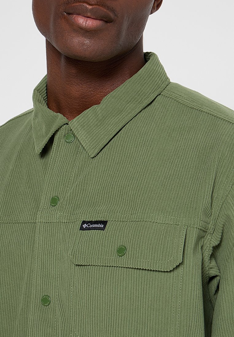 Koszula z kordurowej tkaniny w oliwkowym kolorze z kołnierzykiem zapinanym na guziki, jedną kieszenią na piersi i naszywką z logo. Wykonana z teksturowanej tkaniny z widocznymi żebrami.