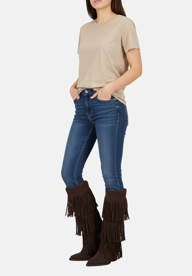 T-shirt beige à manches courtes, jeans bleus ajustés et bottes en suède marron à franges avec des franges superposées et des bouts pointus.