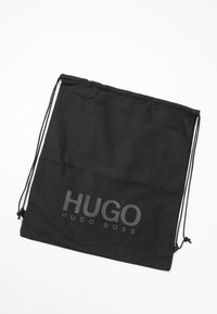 Sac à cordon noir avec le logo «HUGO BOSS» imprimé en gris, étalé à plat sur un fond blanc.