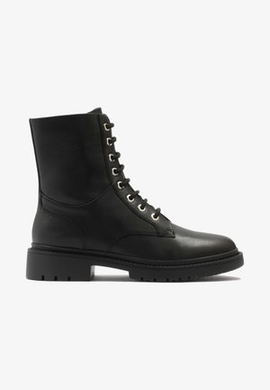 Stivale alla caviglia in pelle nera con punta rotonda, occhielli in metallo, lacci frontali e suola in gomma spessa. Texture liscia, design minimalista.