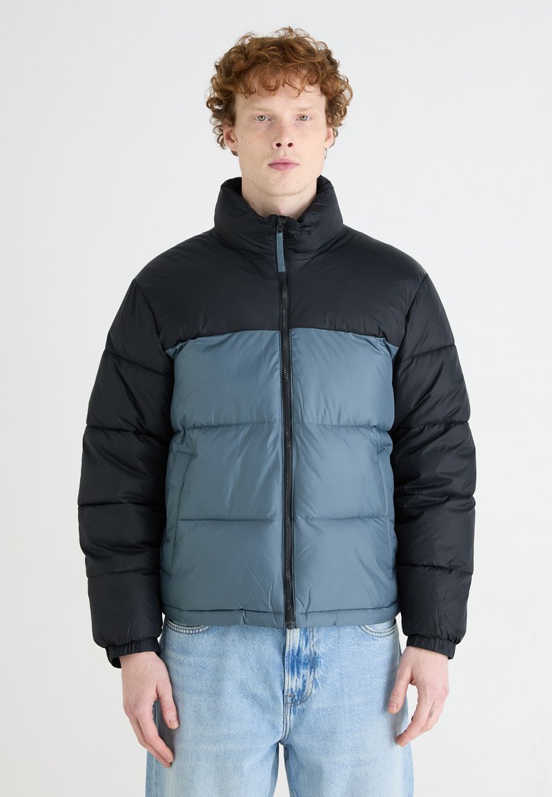 Padded jacket in black and light blue with a high collar, front zipper, and elastic cuffs. Features a smooth texture and segmented design.