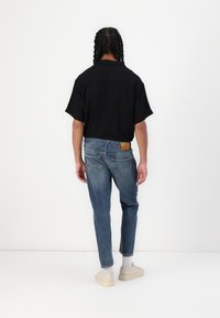 Czarna koszulka z krótkim rękawem w połączeniu z niebieskimi dżinsami. Dżinsy mają tylne kieszenie i jasnobrązową skórzaną łatek na pasku. Na nogach białe trampki.