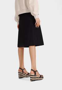 Sandali con tacco a cuneo neri con tomaia in juta intrecciata e tessuto, caratterizzati da un design a righe, cinturini alla caviglia e una suola texturizzata.